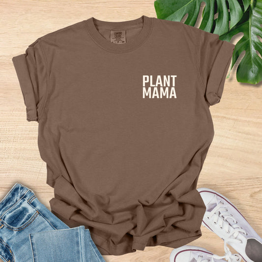 Brown t-shirt with 'PLANT MAMA' text on a wooden surface with jeans and sneakers.