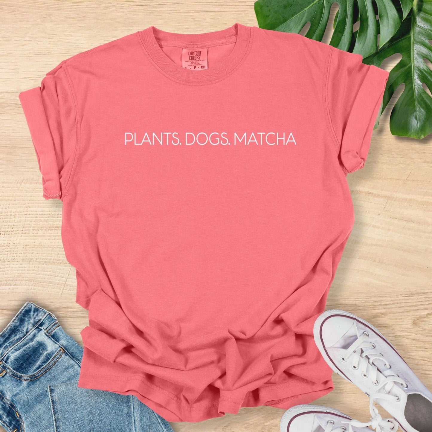 Dark Pink t-shirt with 'PLANTS. DOGS. MATCHA' text on a wooden surface with jeans and sneakers.