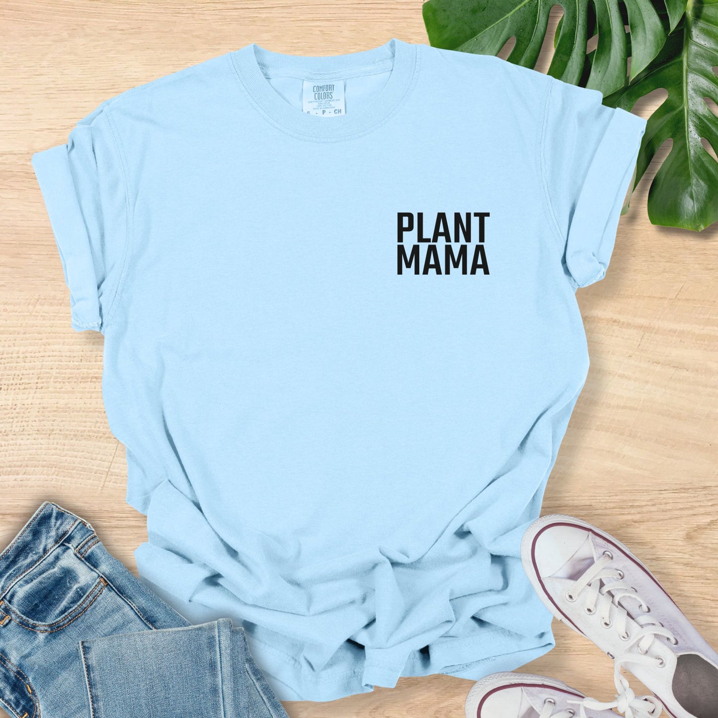 Light blue t-shirt with 'PLANT MAMA' text on a wooden surface with jeans and sneakers.