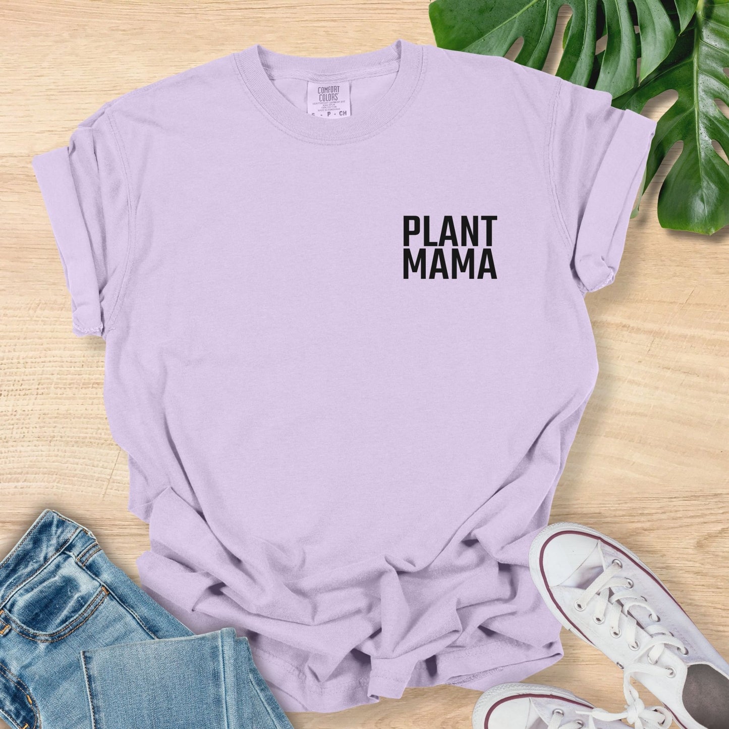 Lavender t-shirt with 'PLANT MAMA' text on a wooden surface with jeans and sneakers.
