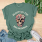 Green t-shirt with skull design and text 'Beauty in the Breakdown' on a wooden surface with jeans and sneakers.